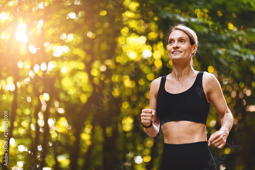 Cuadro en lienzo Smiling Caucasian Woman Running In Nature, Energized And Focused During Outdoor Exercise In Park Setting