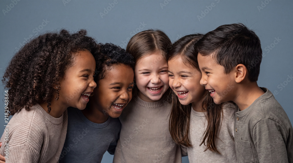 Obraz premium A portrait of a diverse group of multi-ethnic children huddled together, laughing and smiling against a soft blue studio background, representing friendship.