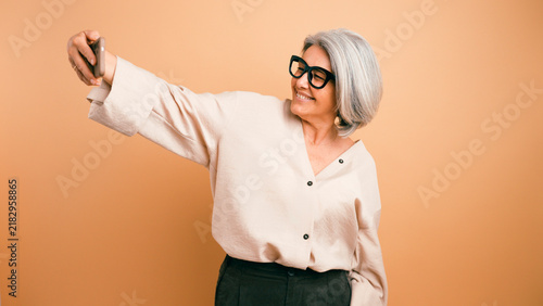 Senior woman smiling and taking a selfie using her smartphone, showcasing modern technology use and happiness in older age