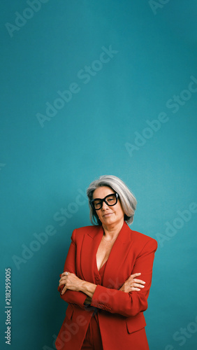 Картината върху платно Senior businesswoman in a red suit and glasses standing with crossed arms, portr