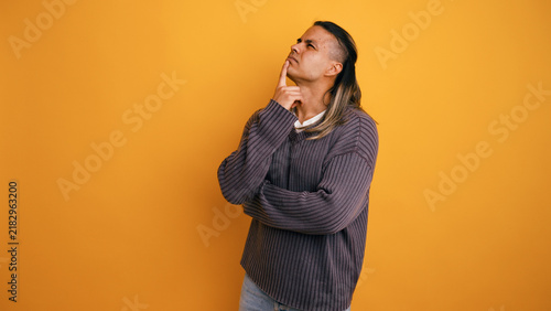 Latino man in a studio setting with a yellow background, deeply contemplating and processing information, showing doubt or curiosity