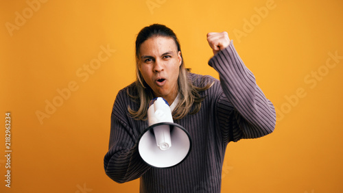 Fotografie Latino man holding a megaphone, an activist, shouting and raising his fist in pr