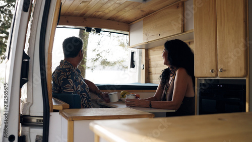 Mature couple relaxing inside a customized camper van, drinking coffee and looking out the window, embracing travel lifestyle