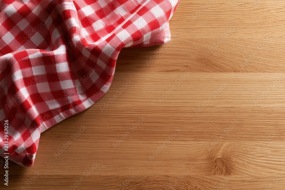 Obraz premium Red and white checkered kitchen towel draped on the corner of a clean natural wood table surface with ample space for text or food display