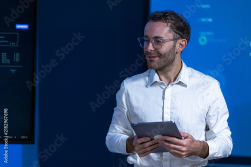 фотографія A young male technology specialist in a soft blue shirt and thin glasses watches