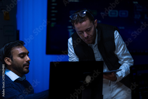 Fotografie A bespectacled male team lead in a dark gilet and rolled white sleeves leans ove