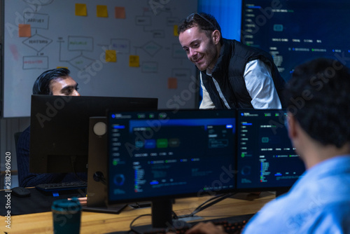 A young male engineer in washed denim concentrating on his screens rests a hand on the mouse while reading through a long log file in a modern data operations centre