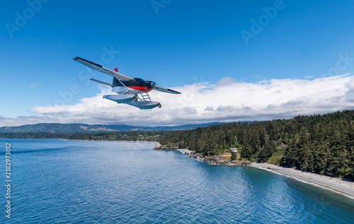 Fotografie Seaplane Floatplane Flying Over Coastal Ocean Near Forested Shoreline With Clear