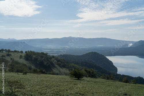 Fotografie Wide caldera lake and rolling green hills in soft morning light