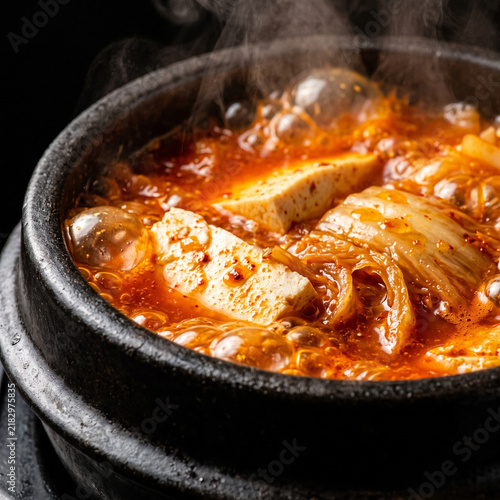 Boiling hot Korean kimchi jjigae stew with tofu and cabbage bubbling in traditional black ttukbaegi stone pot