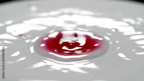 Red liquid drop falling into white surface creating a splash and ripple effect