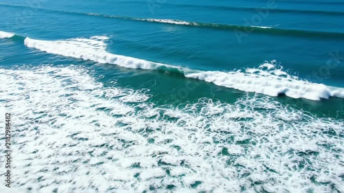 Aerial view of turquoise ocean waves rolling and breaking on the surface of the sea.