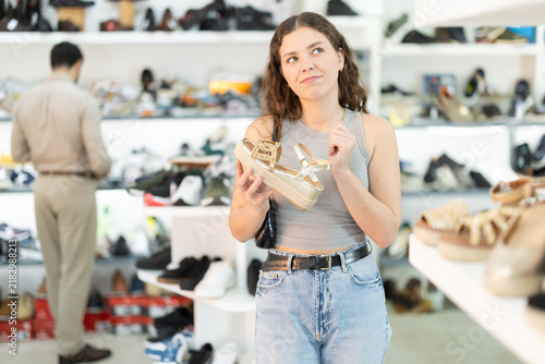 Thoughtful woman stands in a shoe store and chooses platform sandals  she chooses new shoes for a summer dress.