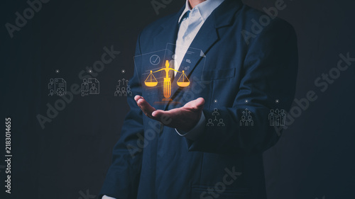 Businessman holding a glowing digital scale of justice hologram with corporate governance. Futuristic corporate technology for legal compliance, business ethics, and labor law.