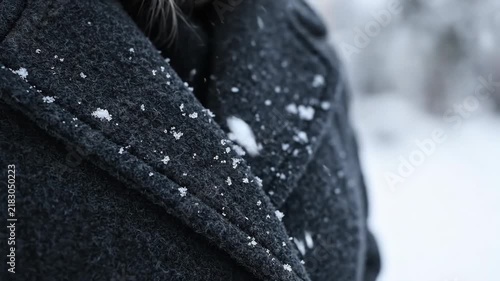 Macro snowflake falling on dark wool coat during winter snowfall