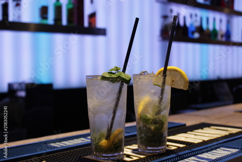 Fotografía Dos vasos de mojito con hielo, menta y rodajas de lima, sobre la barra de un bar con luces de neón de fondo