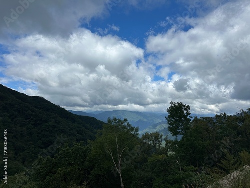 Фотография 울창한 숲과 여러 겹의 산 능선 위로 커다란 구름이 펼쳐진 산악 풍경 사진