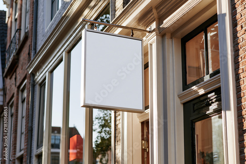 Blank white rectangular shop sign mounted above a storefront doorway