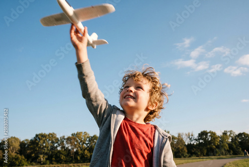 Happy Curly Haired Little Boy Flying a Model Glider Airplane in a Sunny Park, Outdoor Play and Active Childhood