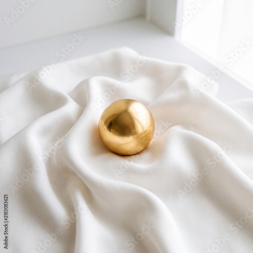 Polished Golden Sphere Resting Centered On Rippling White Silk Fabric Bright Minimalist Flat Lay Luxury Concept