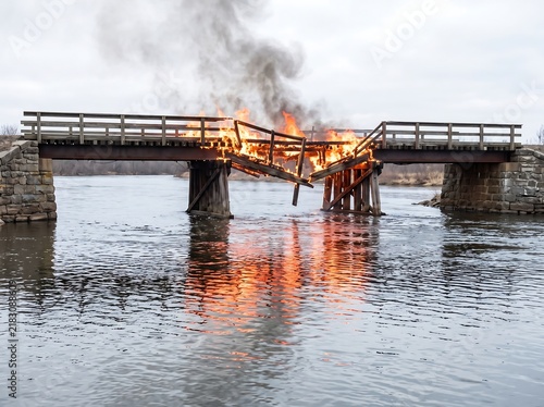 Dramatic fire destroying a wooden bridge over calm river water