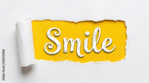 Word smile written on yellow paper behind torn white paper