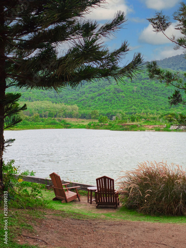 Two Wooden Chairs Facing a Scenic Lake and Mountains in a Lush Green Landscape
