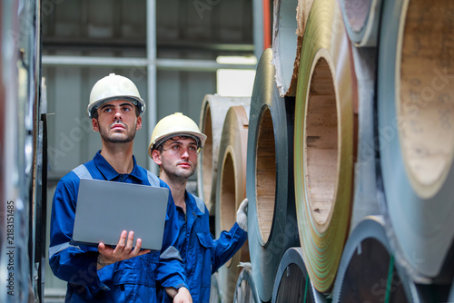 Naklejka Two Caucasian male engineers holding laptop and inspecting steel coils in warehouse
