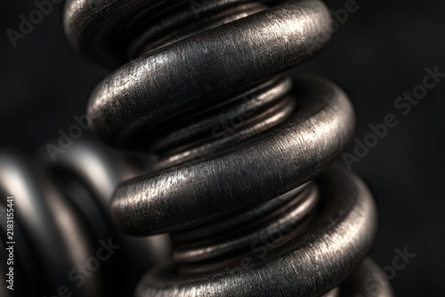 Close-up of a textured metallic helical compression spring with worn steel coils and a dark background.