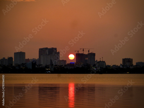 Orange Sun Over Construction Cranes and Waterfront Skyline on West Lake in Hanoi, Vietnam