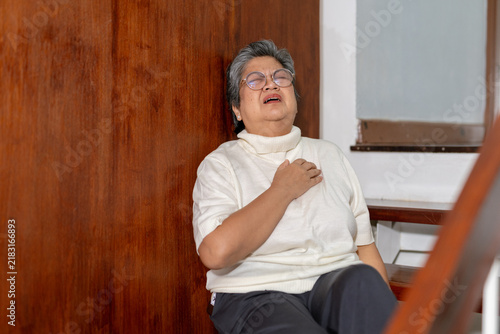 Foto Senior Asian woman clutches chest in severe pain sitting on wooden staircase at