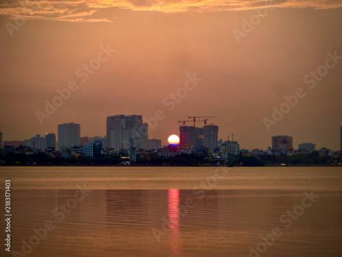 Red Sun Setting Behind City Skyline Across Calm Urban Water on West Lake in Hanoi, Vietnam