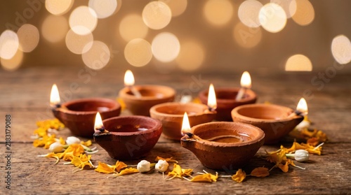 Diwali diyas or clay lamps lit and arranged on wooden surface decorated with flowers with blurred background with bokeh lights