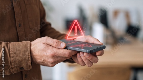 Smartphone with glowing red warning triangle hologram over screen, representing fraud detection, mobile cybersecurity and phishing threat protection in digital banking system.