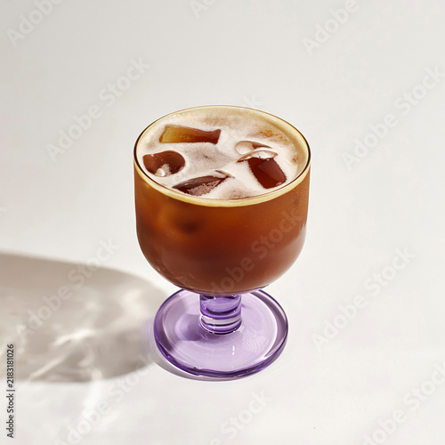 Obraz na płótnie ed shaken espresso with foam and ice cubes in a glass with a purple stem on a wh