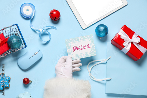 Santa Claus hand with gift card, modern gadgets, gifts and Christmas decorati...