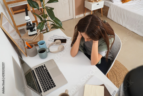 Stressed female student studying at table in room