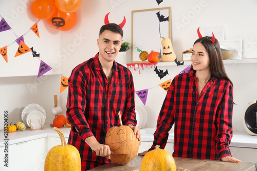 Young happy couple in pajamas carving pumpkin for Halloween party at home
