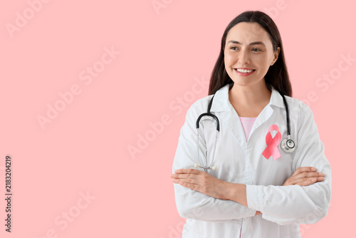 Female doctor with pink ribbon on color background. Breast cancer awareness c...