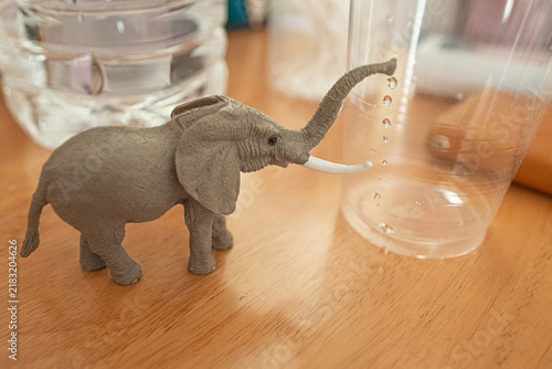 Toy elephant beside clear plastic cups with water droplets on a table
