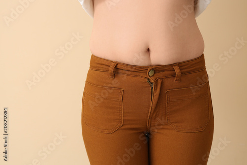 Young woman in tight pants on beige background  closeup. Weight gain concept