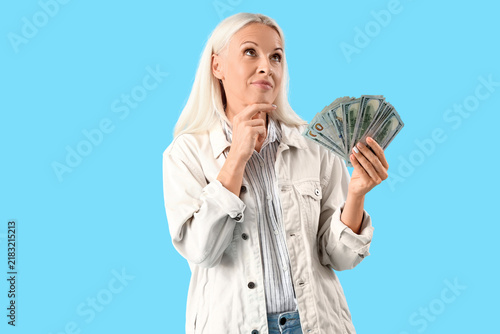 Thoughtful mature woman with dollar banknotes on blue background