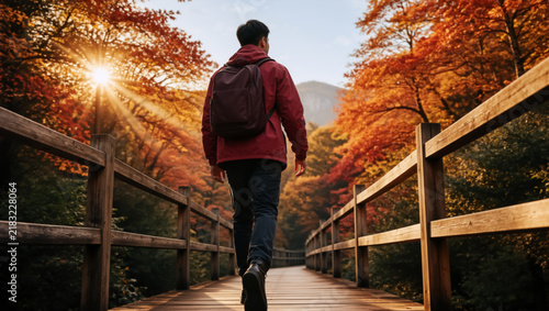 Hiker walking on a wooden bridge in a colorful autumn forest. Person with a backpack exploring nature on a sunny fall day. Outdoor adventure and travel