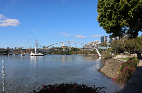 Scenic daytime view of the Goodwill Bridge crossing the Brisbane River, featuring the South Bank parklands shoreline, city apartments, and a clear blue sky in Queensland, Australia