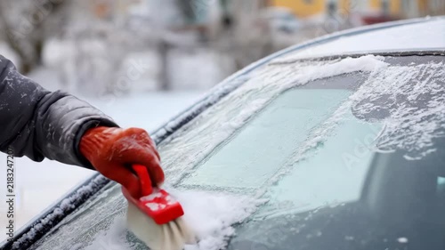 Person clearing snow and ice from car windshield