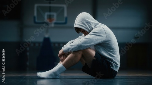 Disappointed young athlete sitting on a basketball court feeling loss and despair.