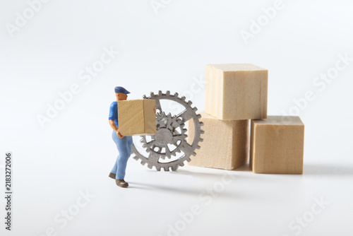 Entrepreneurship and business growth represented by miniature worker carrying a box beside gears and wooden blocks