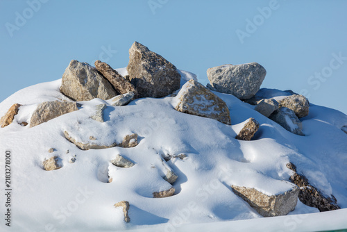 Snow blankets rocky outcrop under clear blue sky. Large, jagged stones protrude from white snow cover.