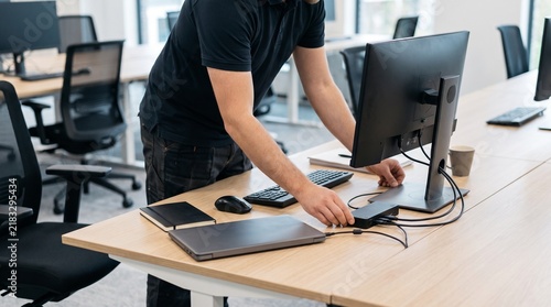 IT technician setting up office workstation with laptop monitor docking station and cables for new employee onboarding and workplace deployment