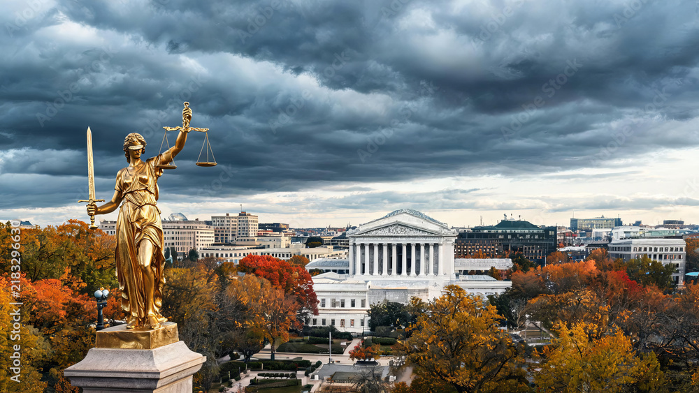 Obraz premium A golden Lady Justice statue overlooks neoclassical government buildings, framed by autumn trees under a stormy sky.